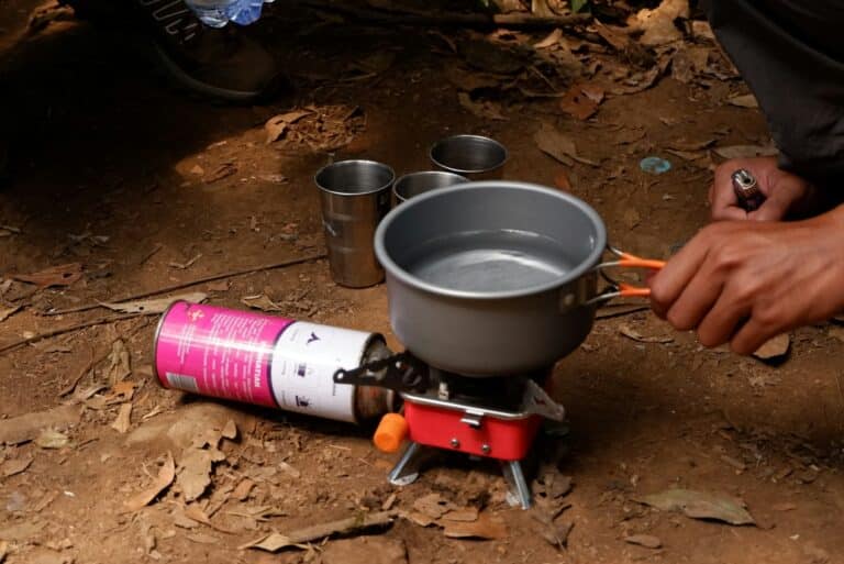 Camper heating water in a metal pot on a portable camping stove