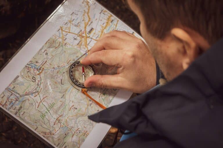 person navigating with map and compass demonstrating traditional wilderness survival skills