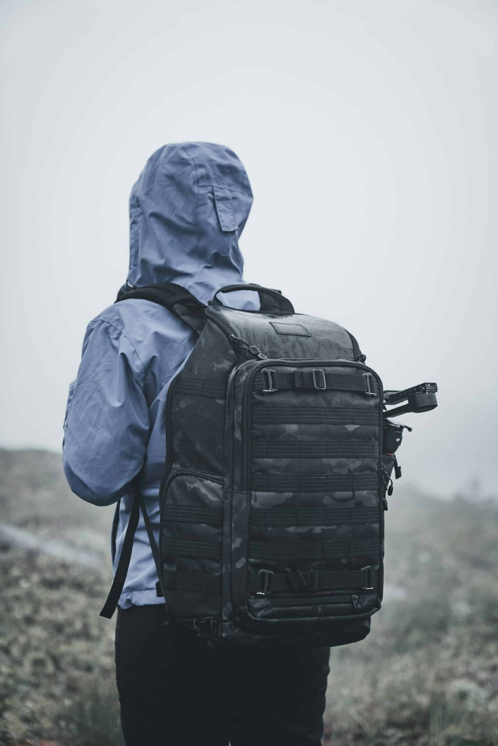 Survivalist wearing tactical bug out bag backpack in foggy wilderness for emergency preparedness.