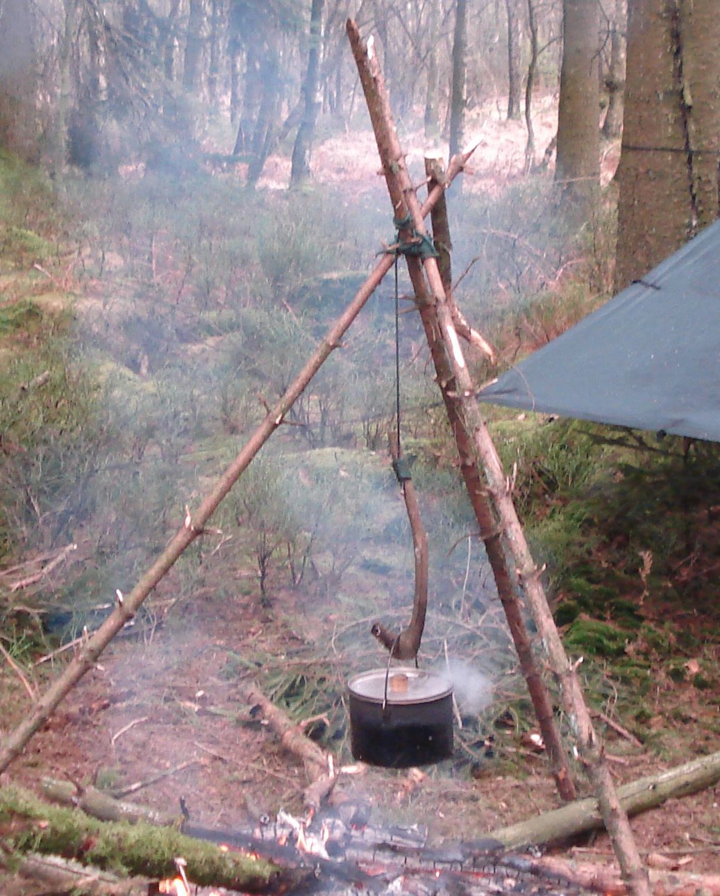 Handcrafted wooden bushcraft tripod holding a pot over a fire in a forest campsite