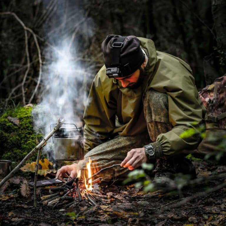 Man building a small survival campfire in the forest while boiling water during wilderness survival.