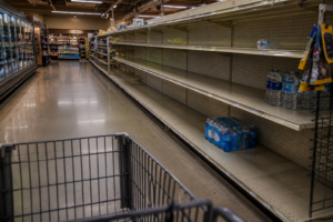 Empty grocery store shelves with only a few cases of bottled water remaining during an emergency supply shortage