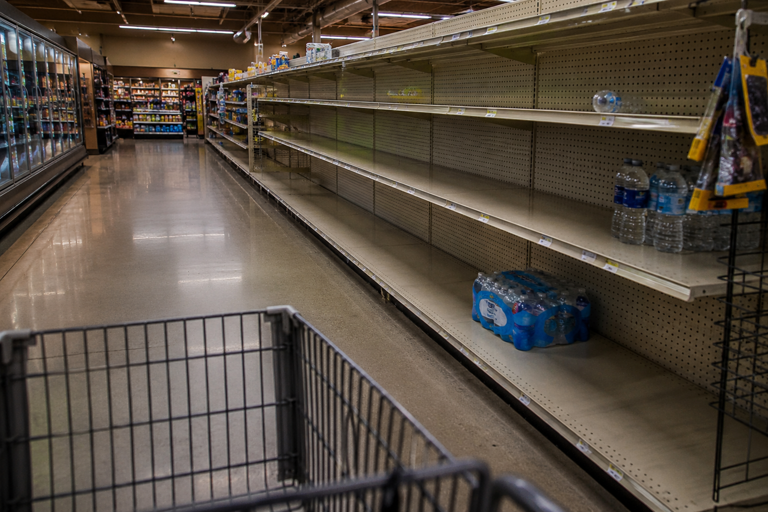 Empty grocery store shelves with only a few cases of bottled water remaining during an emergency supply shortage