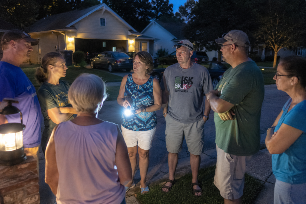 Neighbors gathered on a suburban street during a power outage, using flashlights and lanterns to discuss emergency plans and share information in a neighborhood preparedness meeting.