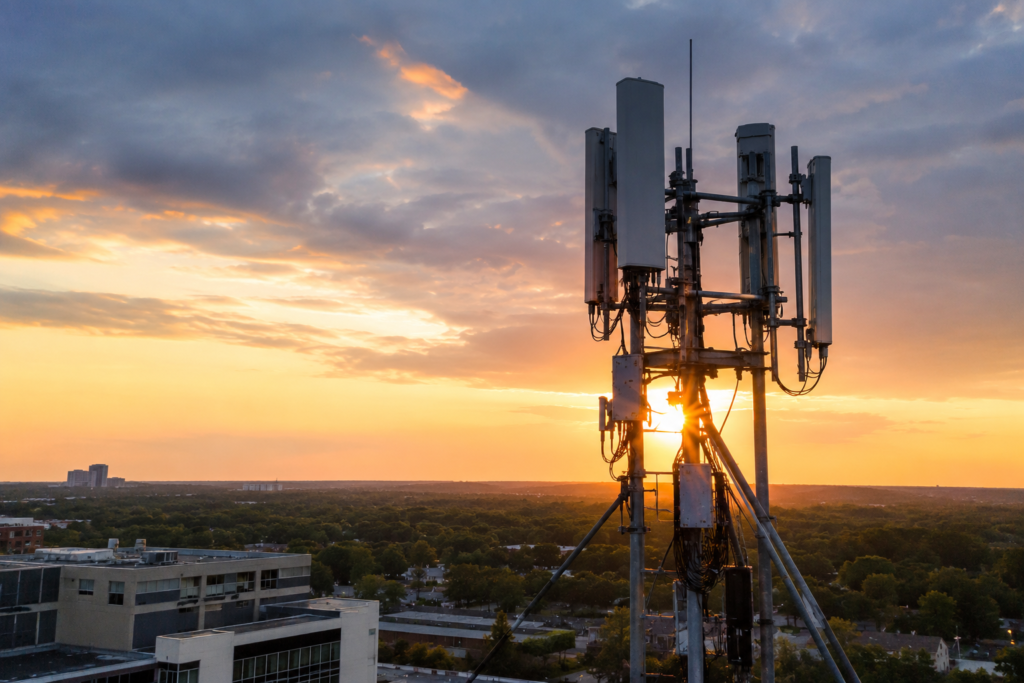 Cell tower antennas operating above a city skyline at sunset, illustrating cellular communication infrastructure and backup network systems during a power outage or blackout.