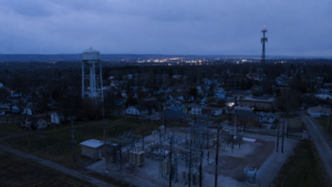 Electrical substation, municipal water tower, and cell tower overlooking a town during a localized infrastructure outage.