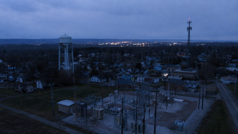 Electrical substation, municipal water tower, and cell tower overlooking a town during a localized infrastructure outage.
